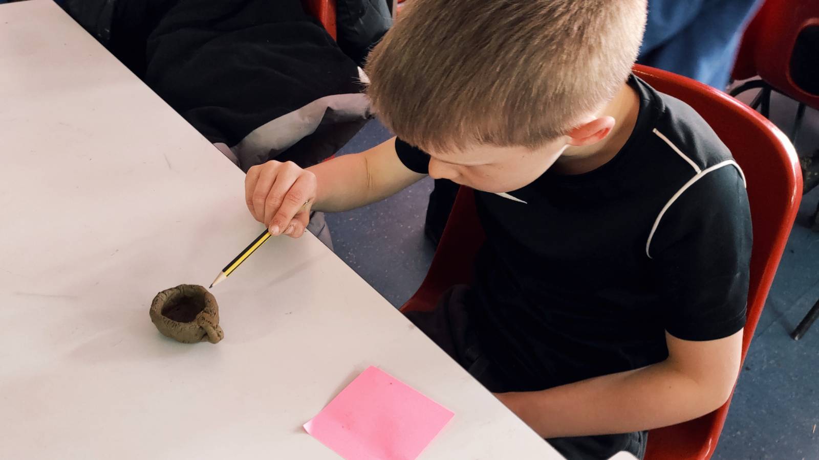 Back in the classroom, student adding a pattern to their tea cup with a pencil.