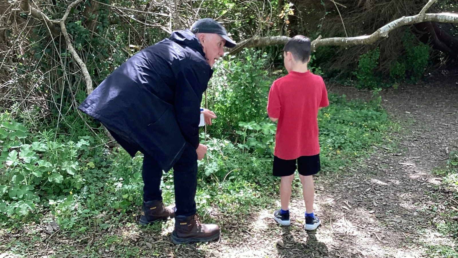 Jake crouching down to talk plants with student in the woodland area