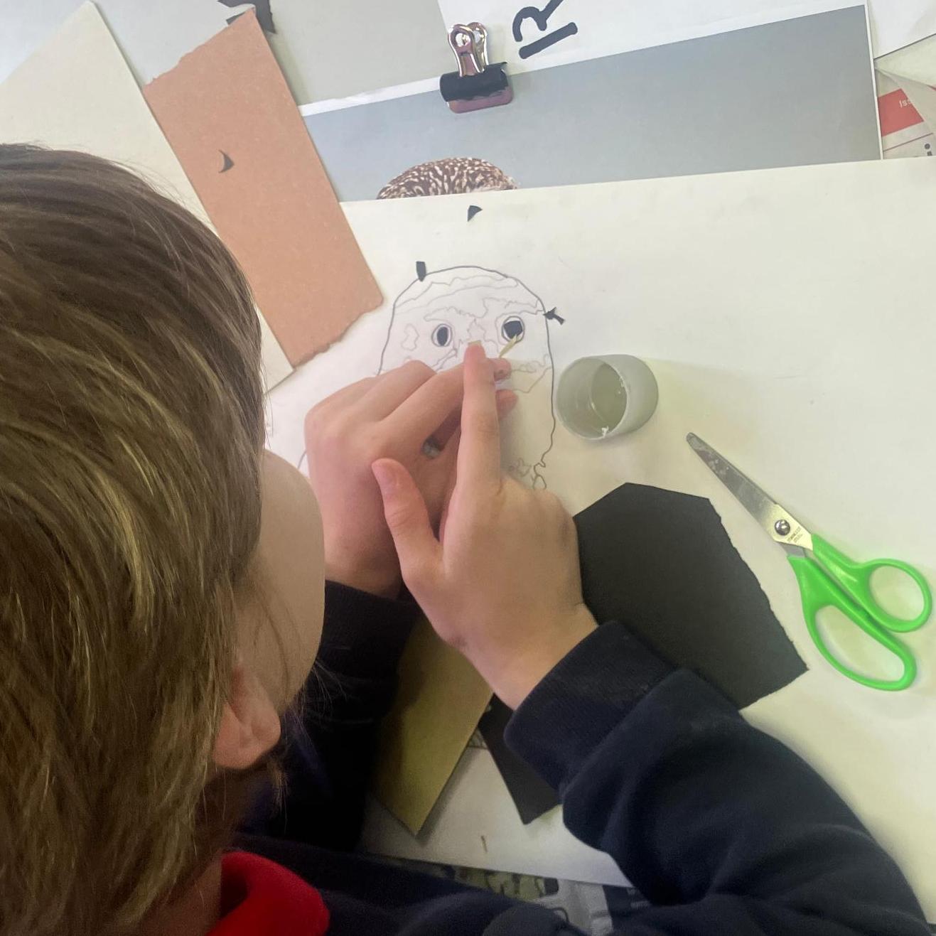 Student adding eyes to the beginning of a collage of a Little Owl / Tylluan Fach