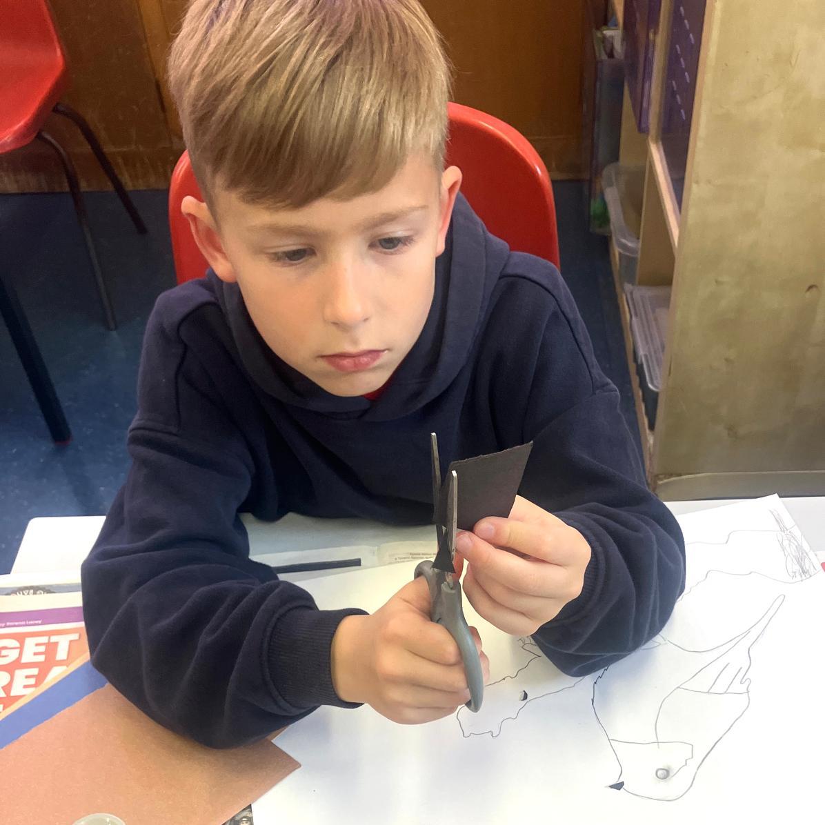 Student very focussed on cutting a piede of card with a pair of scissors
