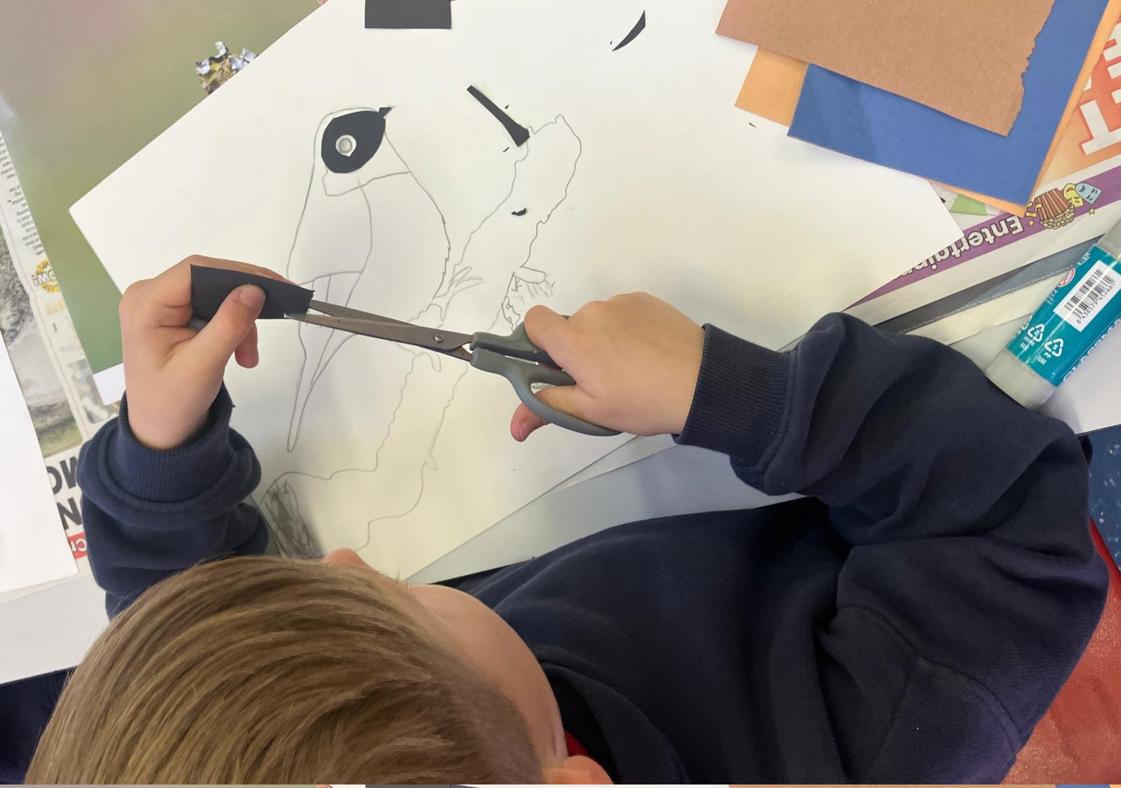 Student cutting out black card with scissors, to begin a collage of a dark headed bird