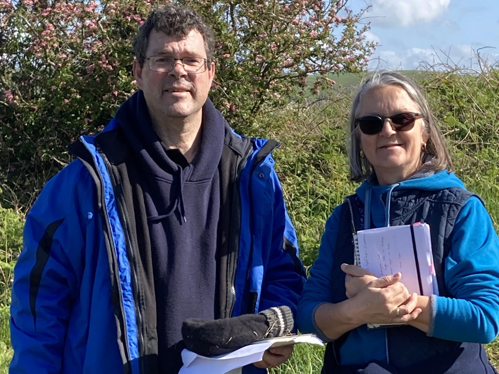 Two people in outdoor gear, in the sun, clasping paperwork