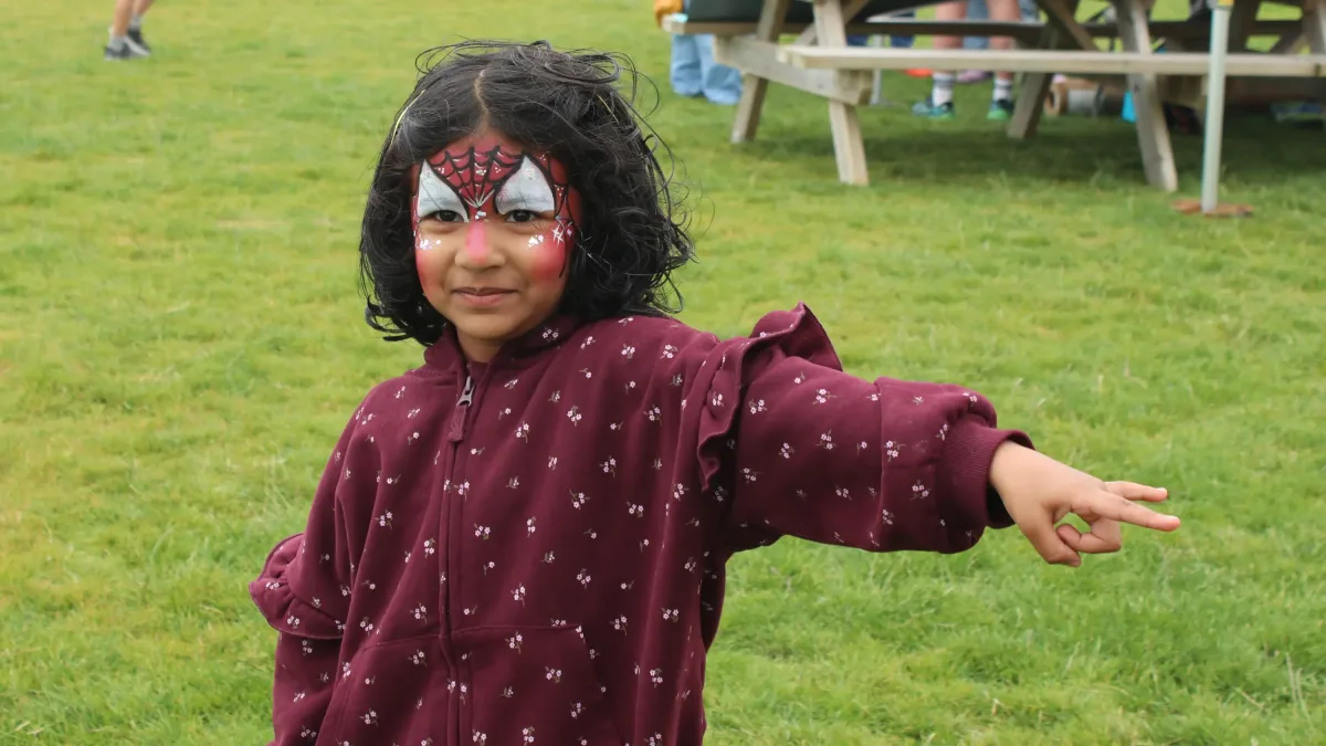 Young person with face painted like Spider-man, with hand outstretched showing their web slinging technique