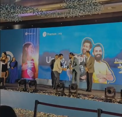 Apex Vouchers receiving Pearson PTE Best Partner Award on stage from brand ambassador Vicky Kaushal