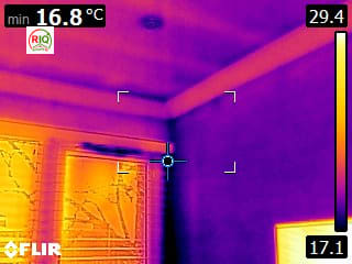 FLIR thermal imaging survey of a wall-to-ceiling corner showing a thermal bridge and cold pipe run — East London