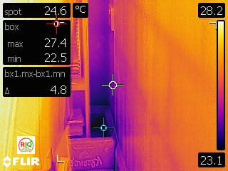 Thermal image showing a dark purple cold spot in the corner of a room, contrasting with the warmer orange walls.