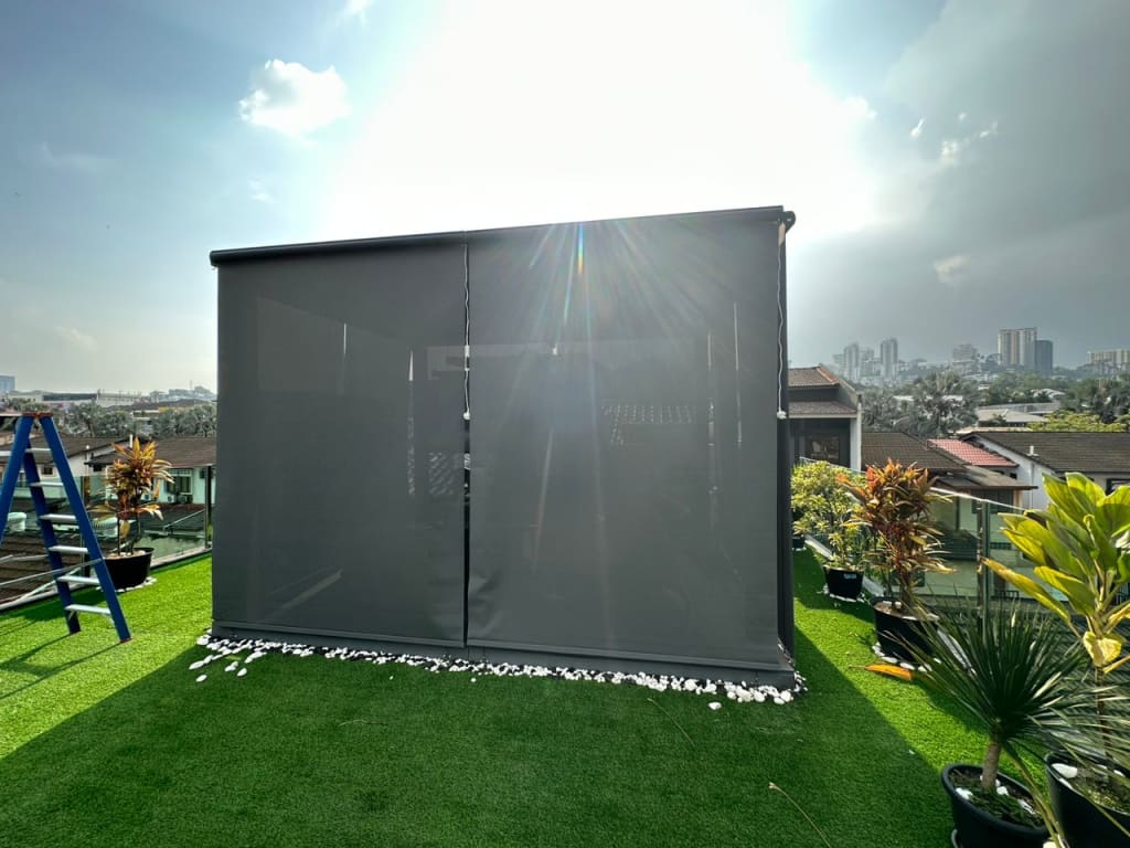 Charcoal outdoor blind fully down enclosing a corner of an artificial-grass rooftop terrace with city skyline behind