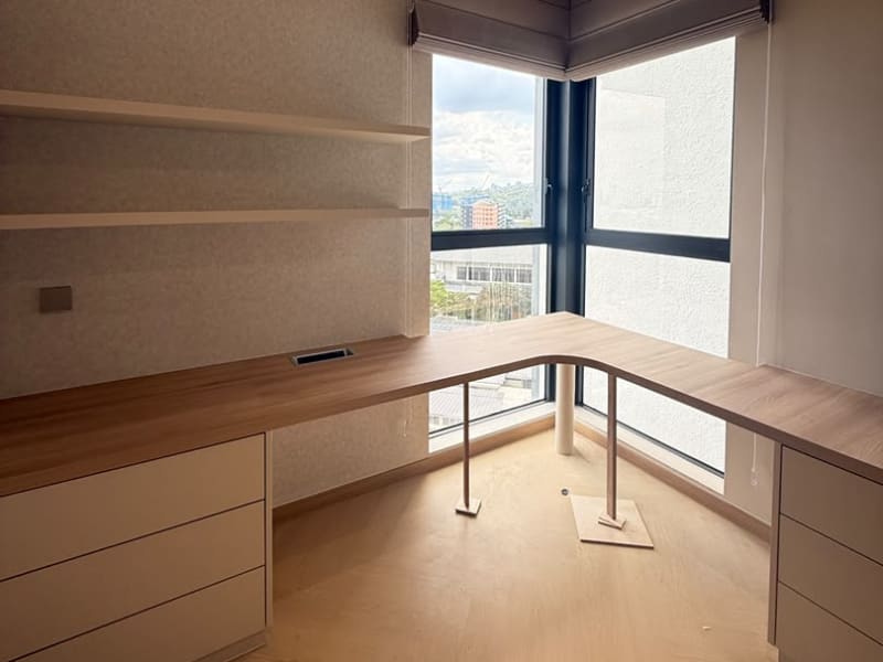 Charcoal roman blind partly lowered over a corner office window with a city view and desk below