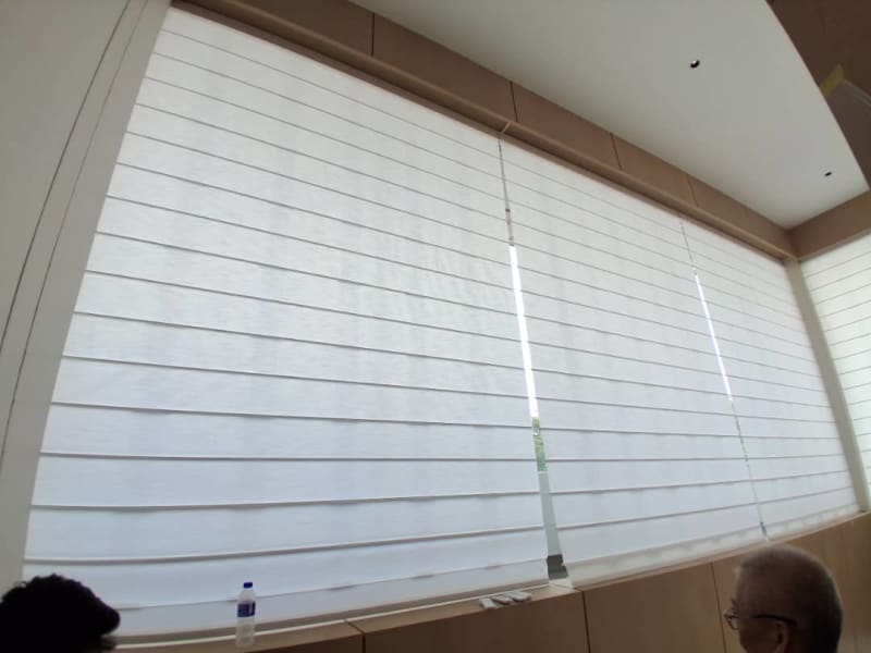 White roman blind lowered over the same sunlit window bench, framed from a different angle