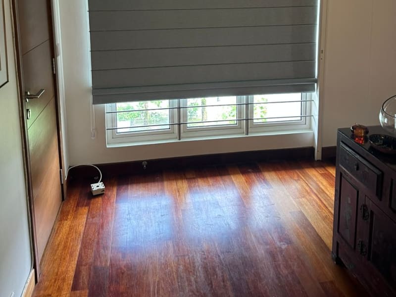 Sage green roman blind lowered over the top of a tri-pane hallway window with greenery visible through the open lower panes