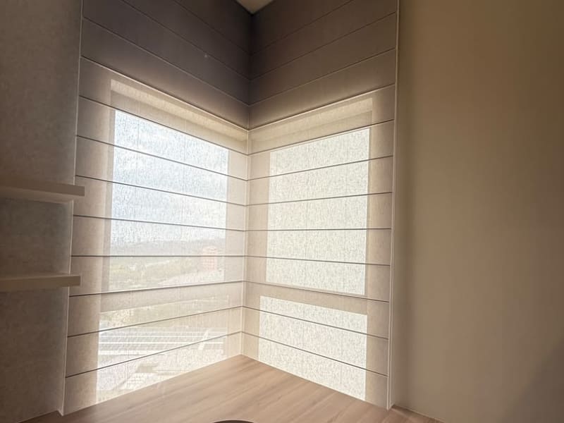 Roman blind partly lowered over a corner office window, seen close up with light shining through the fabric weave