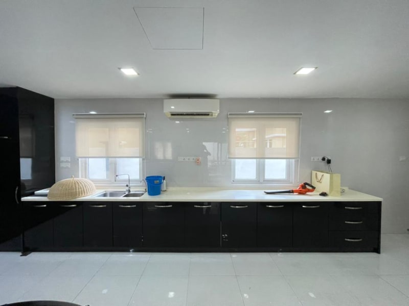 cream light-filtering roller blinds lowered over two kitchen windows above a black countertop, softening the outdoor view
