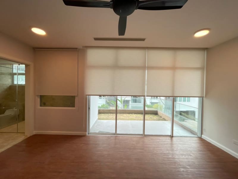 cream light-filtering roller blind lowered over the same sliding door, patio and greenery visible through the glass below