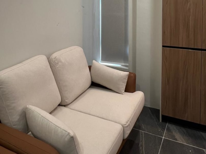 textured light gray roller blinds lowered over a narrow vertical window beside a beige sofa