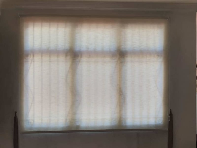 textured sunscreen roller blinds lowered over a window, cordless tension weights on each side, mullions faintly visible