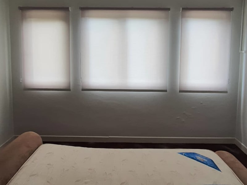 cream light-filtering roller blinds lowered across three separate bedroom window panels, diffusing daylight evenly