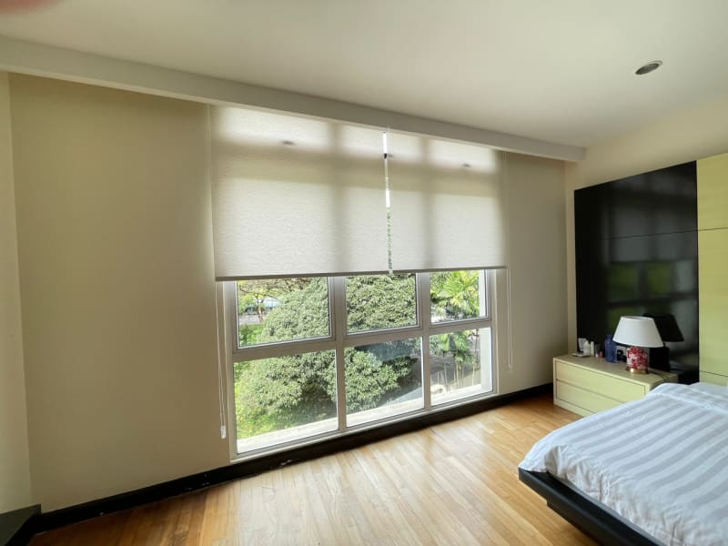 light-filtering roller blind partly lowered over the top of a bedroom window, bead chain hanging at the side