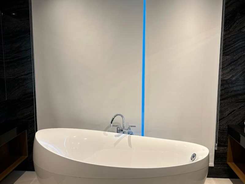 white dim-out roller blind lowered fully behind a freestanding tub, a blue accent light crossing the fabric