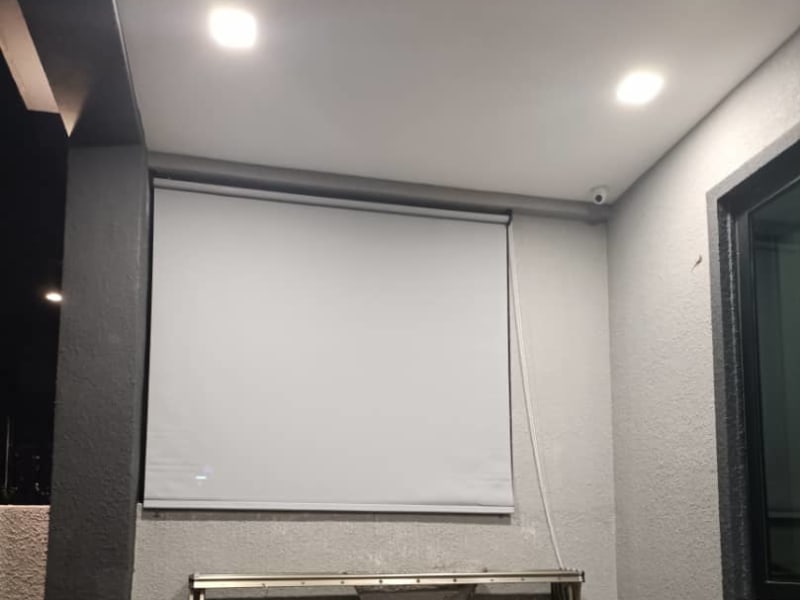 white roller blind lowered over a covered patio at night, a motor mounting bracket fixed below
