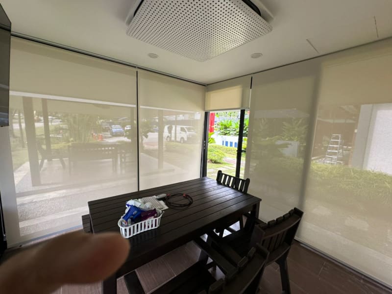 beige sunscreen roller blinds lowered around a dining area, parked cars and a covered walkway visible through the mesh