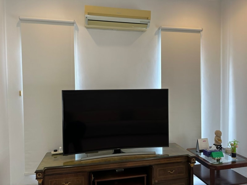 white blackout roller blinds lowered on either side of a wall-mounted air conditioner above a TV console