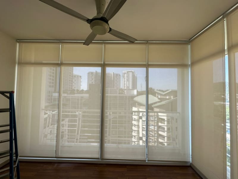 beige sunscreen roller blinds lowered across floor-to-ceiling windows, high-rise buildings visible through the mesh