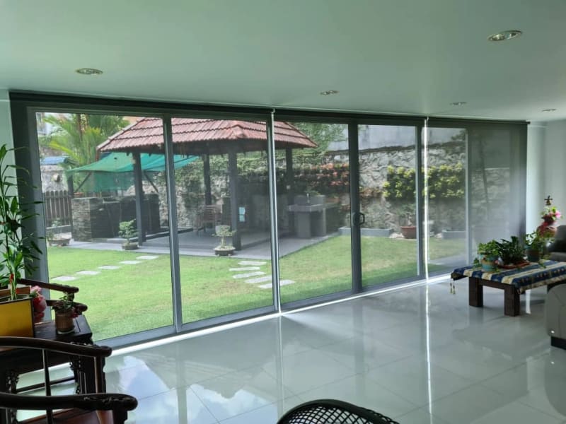 charcoal sunscreen roller blinds lowered across sliding glass doors, garden and gazebo visible through the mesh weave