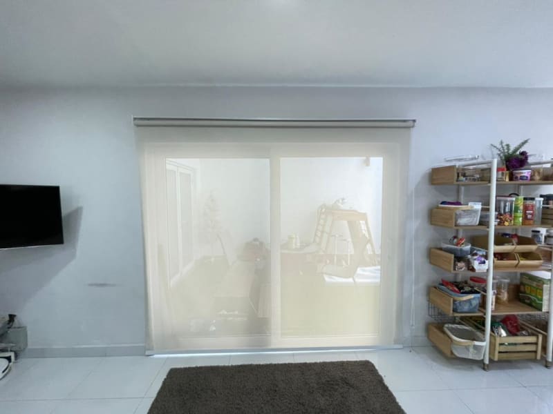 cream light-filtering roller blinds lowered over a sliding glass door, furniture silhouettes visible through the fabric