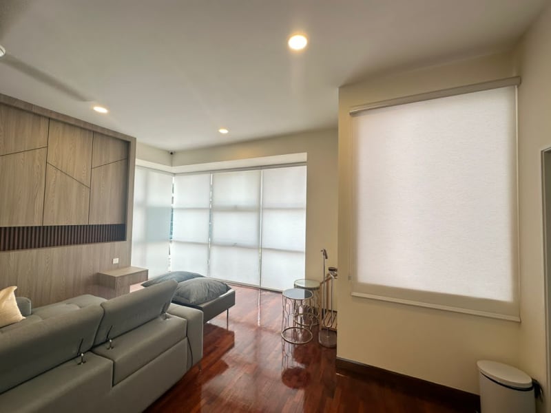 cream light-filtering roller blind lowered over a wall window in the same living room, corner blinds visible behind