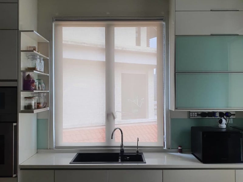 white sunscreen roller blinds lowered over a kitchen sink window, a neighboring rooftop visible through the mesh