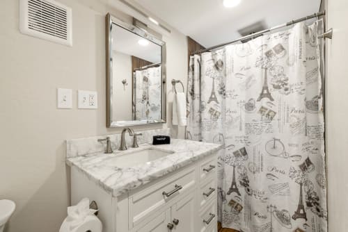 The Master bathroom boasts a spacious walk-in shower,  vanity sink with granite countertop, and elegant tile work, all illuminated by soft, ambient lighting .