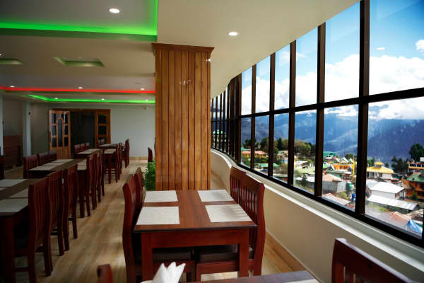 Restaurant dining area with glass window wall framing Tawang mountain valley views.