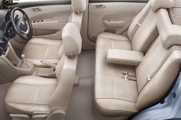 Maruti Suzuki Dzire passenger cabin featuring plush beige fabric seats, rear central armrest with cup holders, and ergonomic legroom.