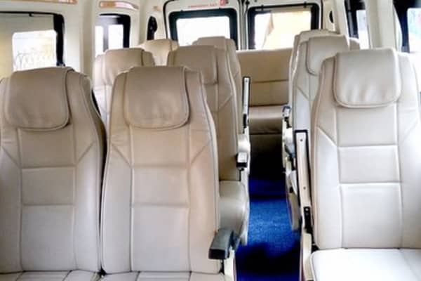 Force Tempo Traveller luxury cabin featuring individual beige leather pushback reclining seats, armrests, and central carpeted aisle.