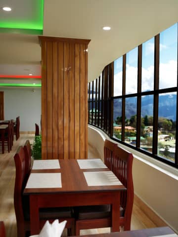 Restaurant dining area with glass window wall framing Tawang mountain valley views.