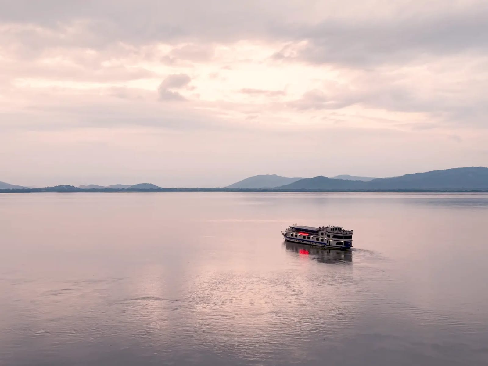 High aerial perspective of Alfresco Grand cruising calm Brahmaputra waters framed by distant hills.