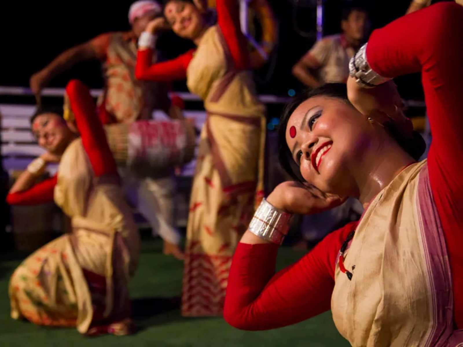 Female Bihu dancers clad in traditional silk mekhela chador performing gracefully on the cruise stage.