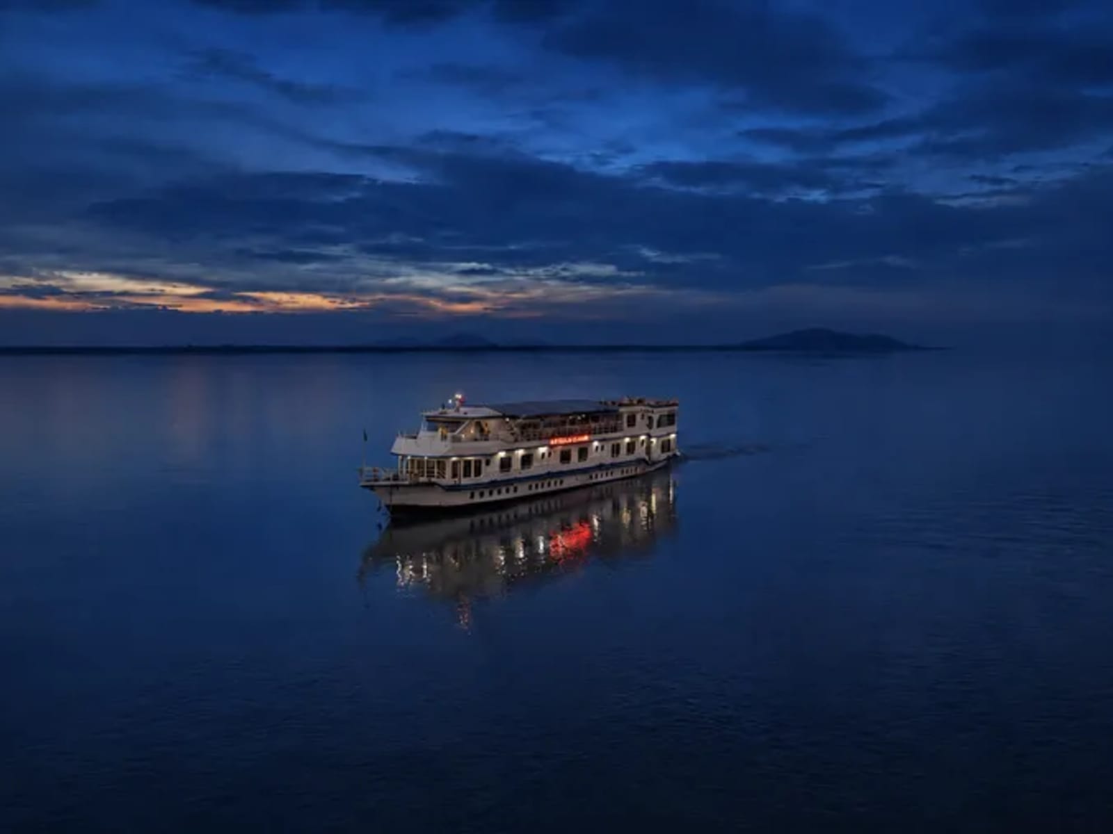 Illuminated vessel glowing on dark blue river water with vibrant reflections during an evening cruise.