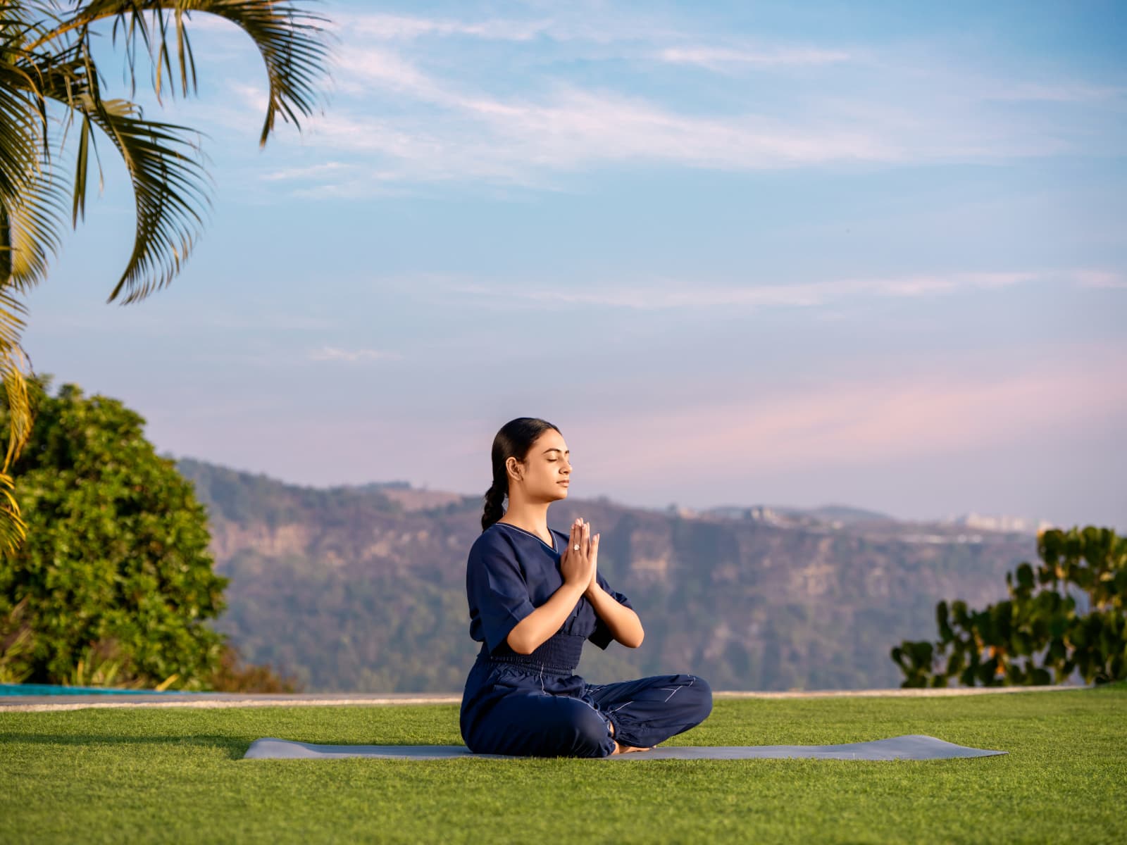 Woman practicing yoga in lotus pose on a green lawn mat facing the dramatic mountain gorge of Cherrapunji