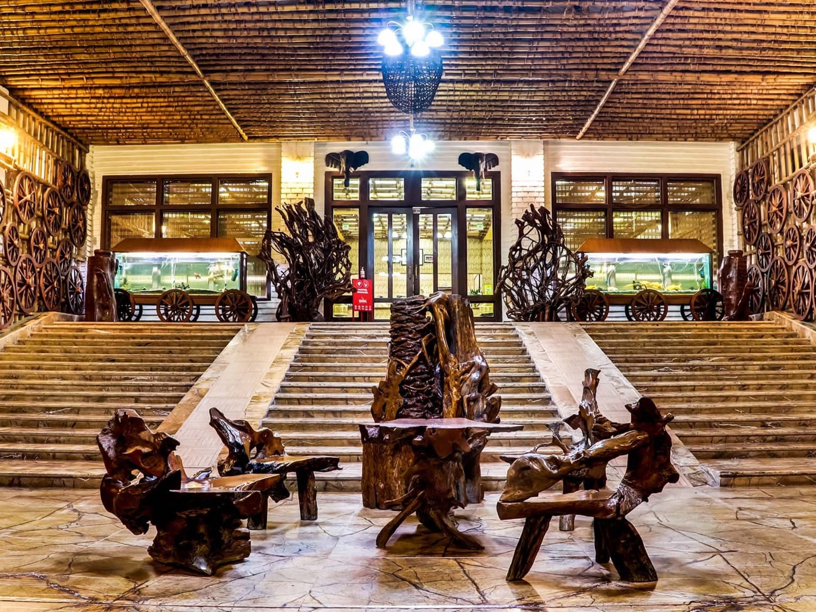 Grand resort lobby foyer featuring bamboo slatted ceiling, wheel wall decor, carved root seats, and aquariums