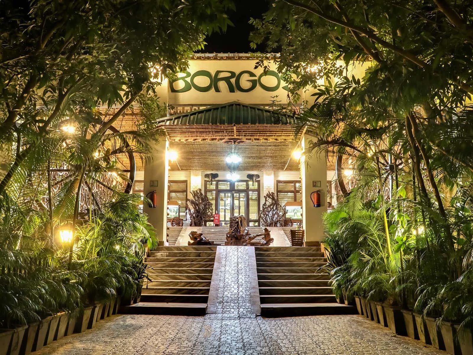Night illuminated stone entrance steps leading to lit BORGOS sign and tropical greenery at Borgos Resort