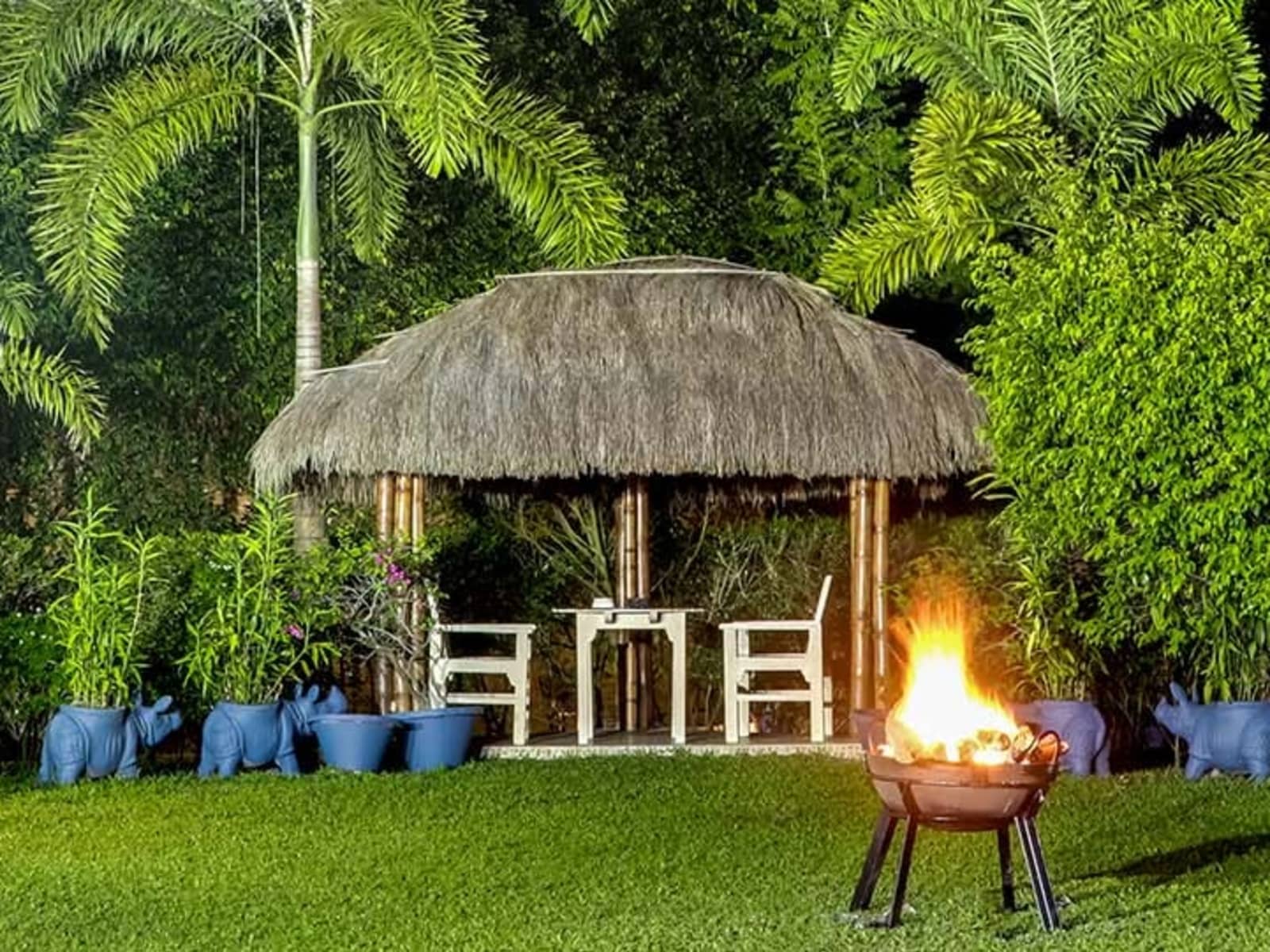Night resort lawn featuring a blazing bonfire pit, thatched bamboo gazebo, and rhino garden sculptures at Borgos