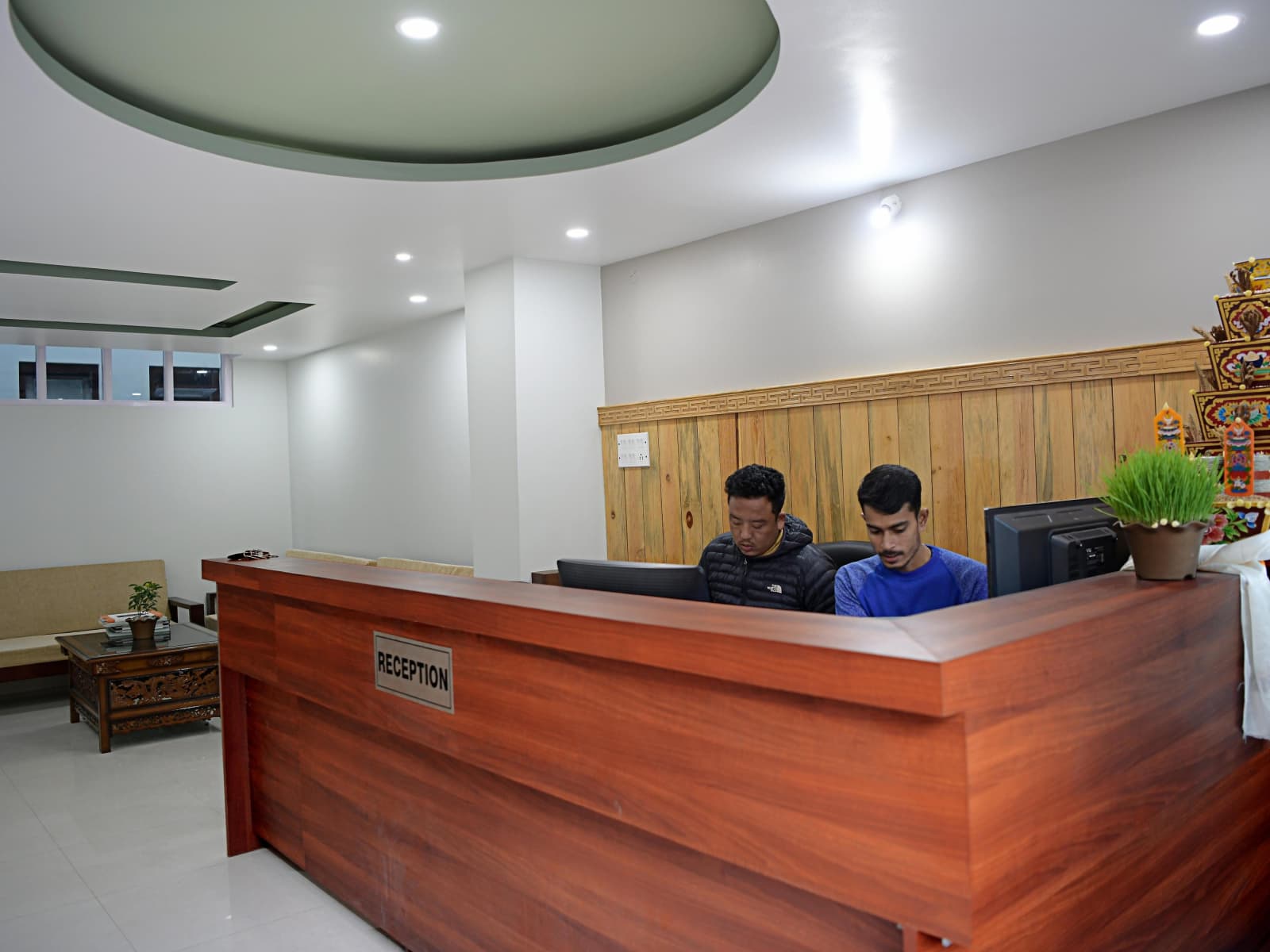 Teak wood reception desk counter with receptionist workstation and decorative shrine.