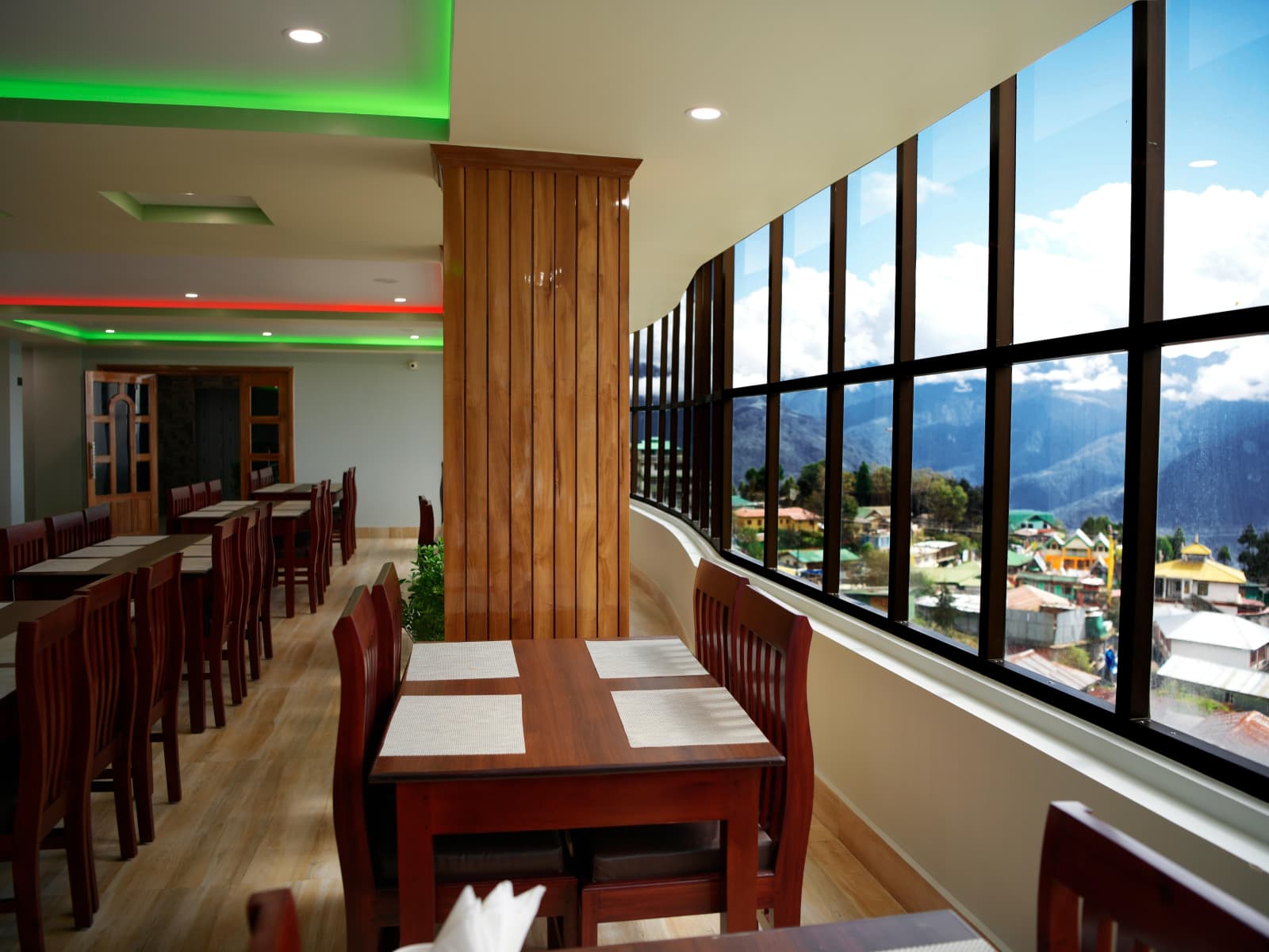 Restaurant dining area with glass window wall framing Tawang mountain valley views.