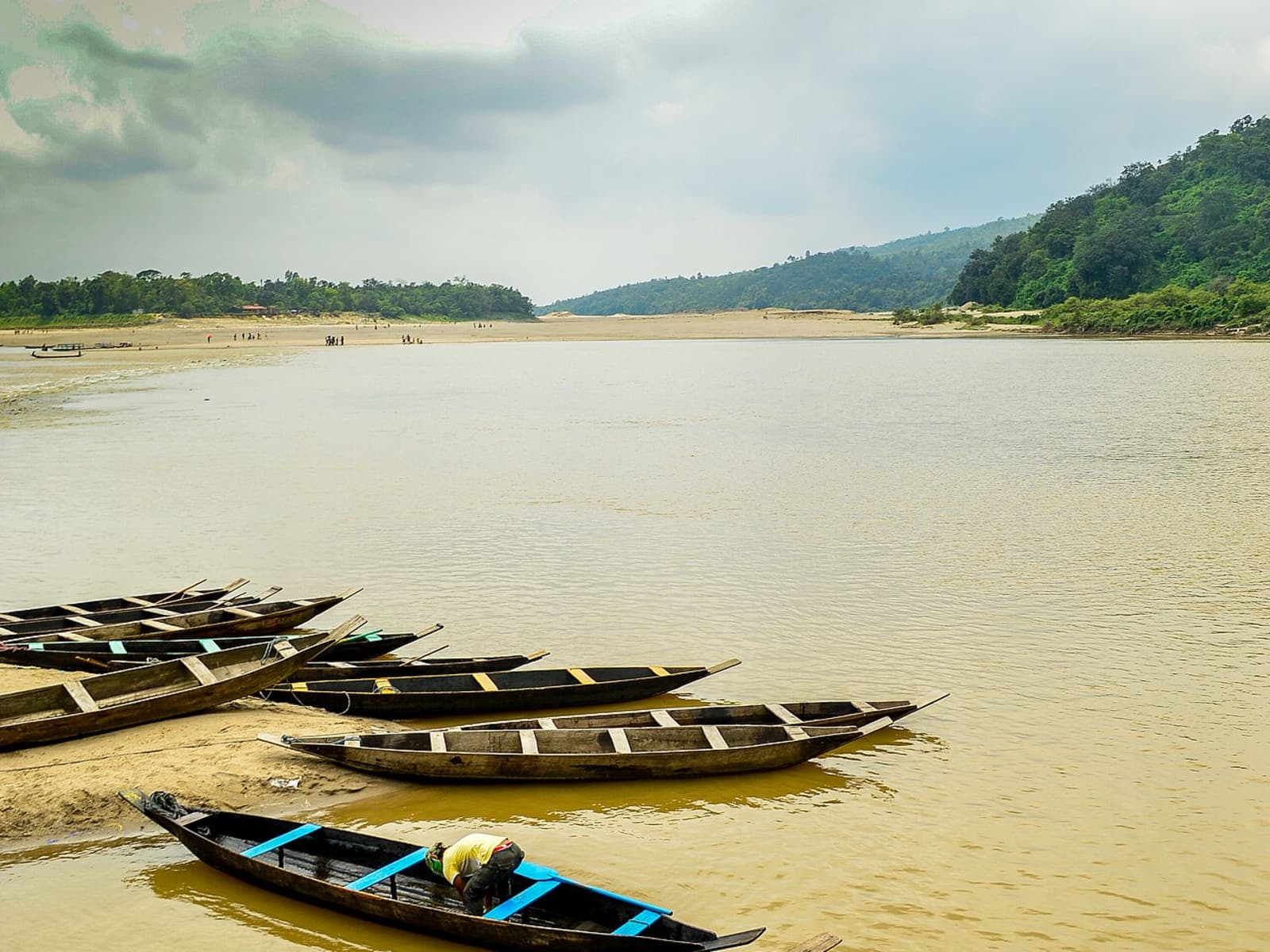 Multiple wooden country canoes lined up along a rocky riverbank under overcast skies.