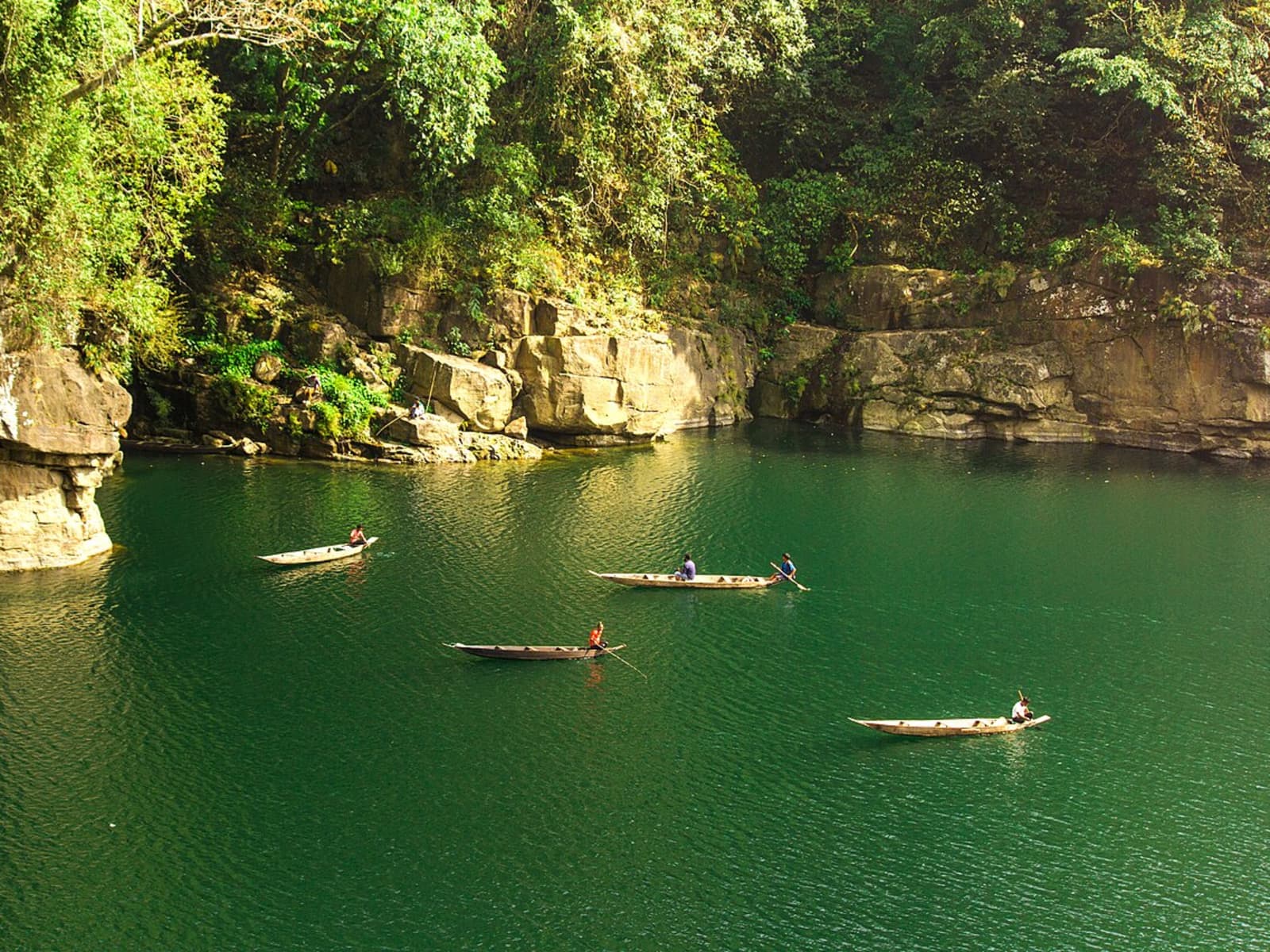 Fishermen rowing wooden boats across deep emerald green river water surrounded by limestone cliffs.