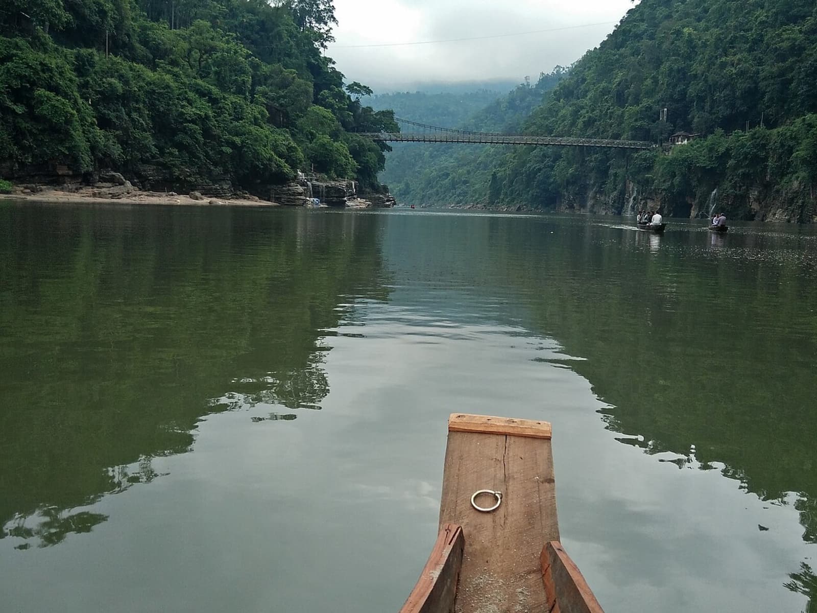 Vertical view from a wooden boat prow looking up the Umngot river gorge toward the suspension bridge.
