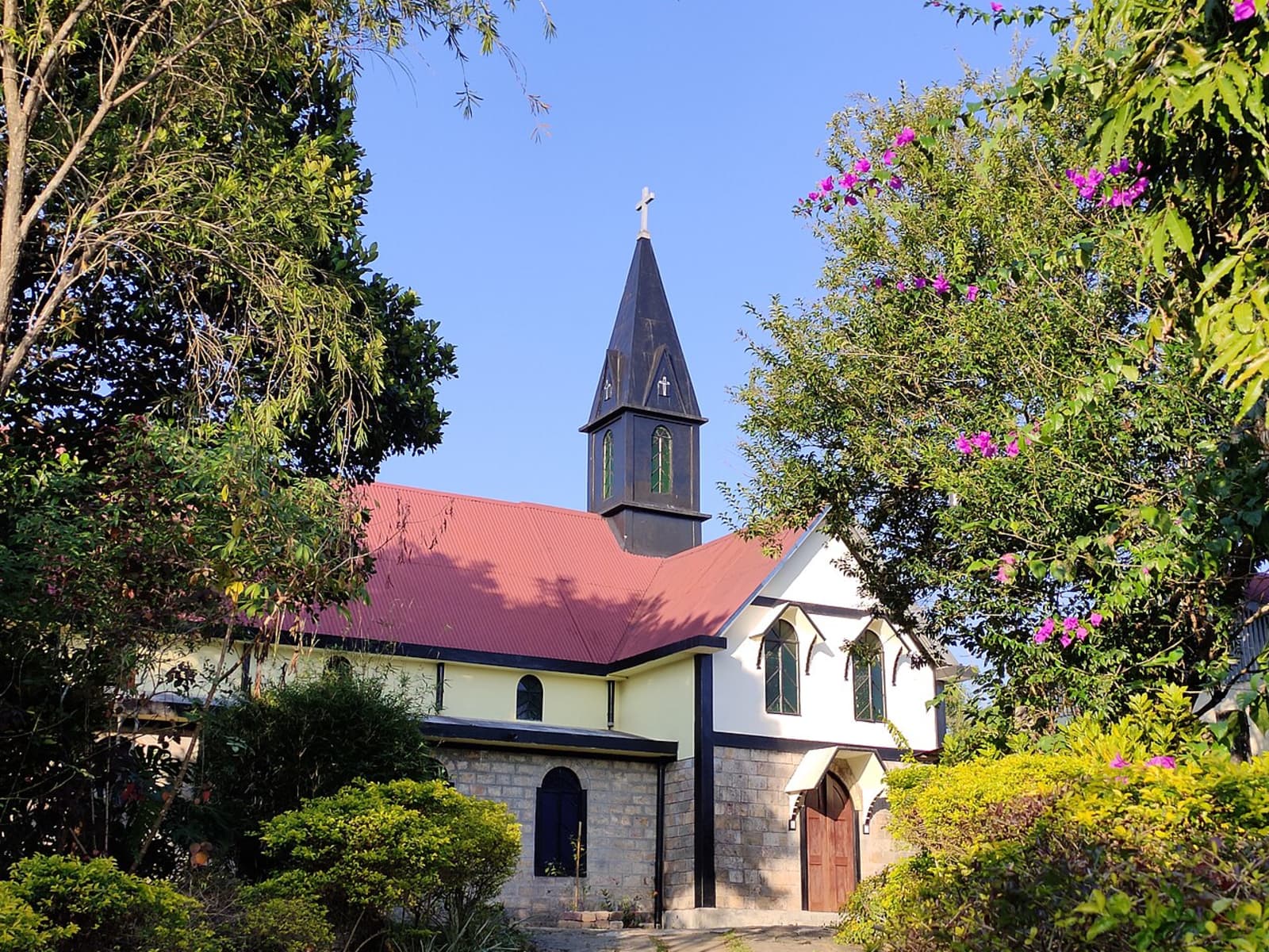Church of the Epiphany showcasing a dark wooden spire steeple red roof and garden path in Mawlynnong village.