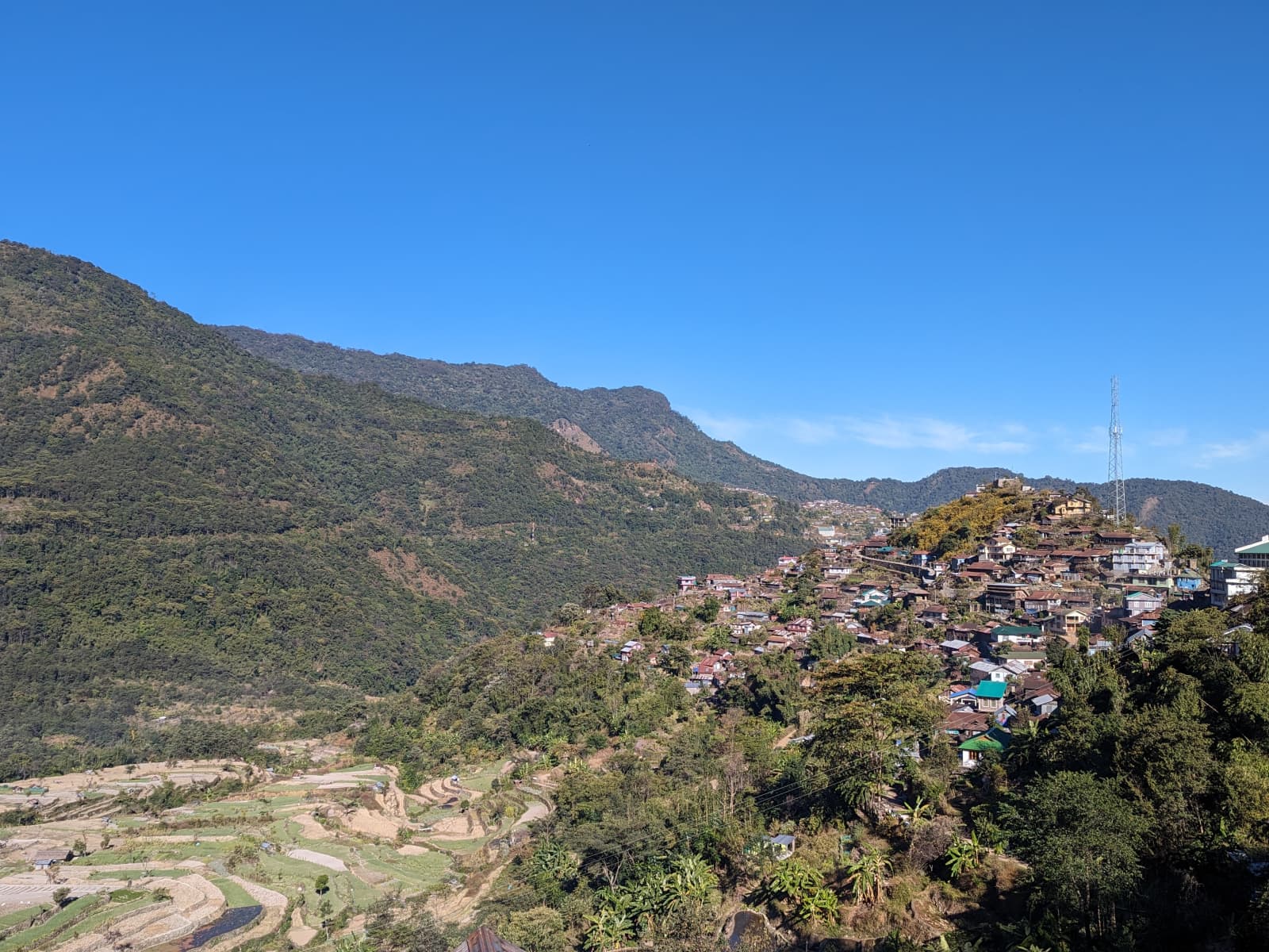 Wide panoramic view of Khonoma village perched along a mist-shrouded mountain ridge in Nagaland