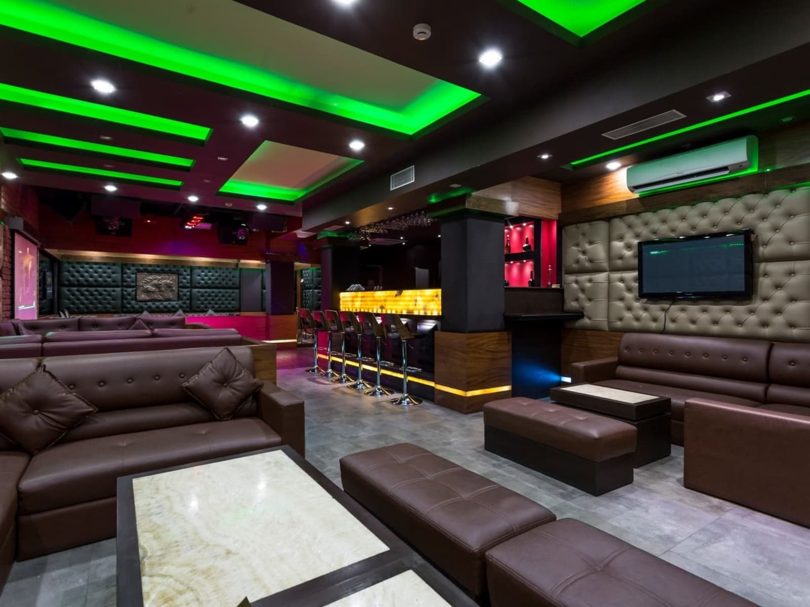 Bar lounge featuring tufted leather sofas, high bar counter stools, and green ambient ceiling lighting.